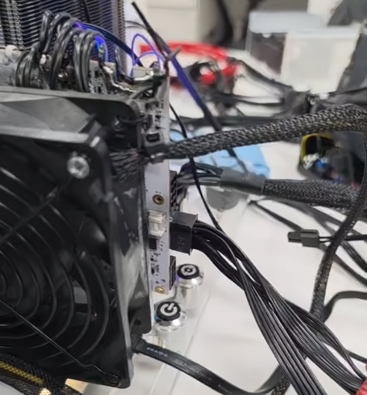 A close-up of a PC build featuring a large cooling fan, multiple cables connected to a GPU, and a visible 'G' logo on a metal stand.